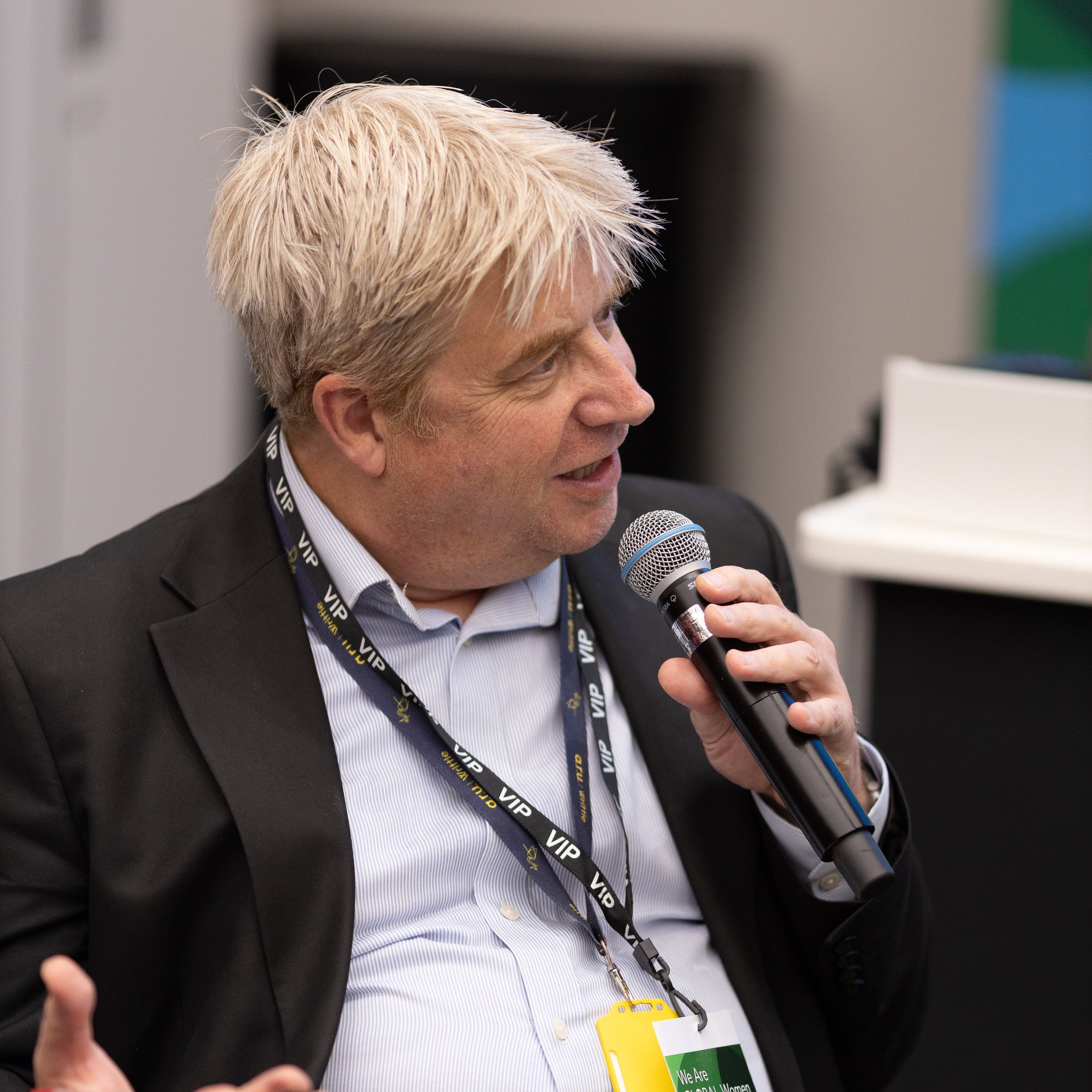 Man speaking into a microphone at an event with a blurred background