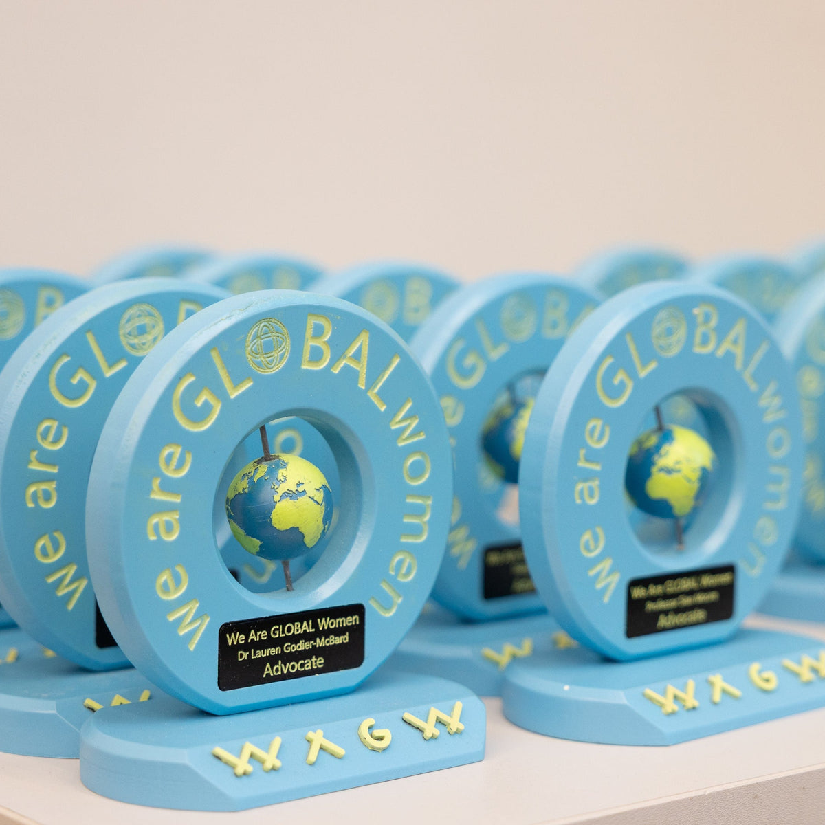 Blue awards with 'We are GLOBAL Women' text and a globe design on a white surface.