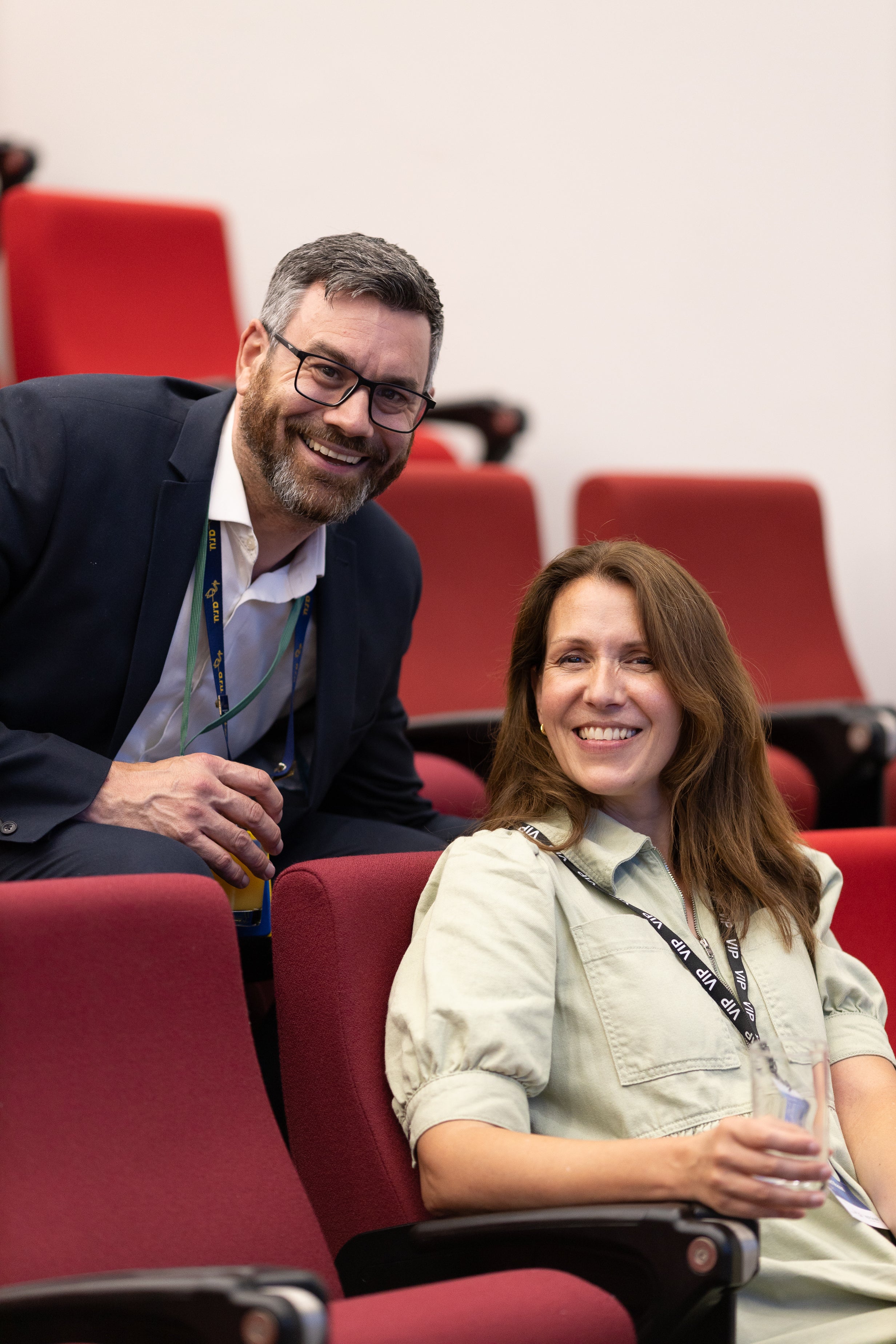 Man and Woman sat in red theatre chairs at an event smiling together