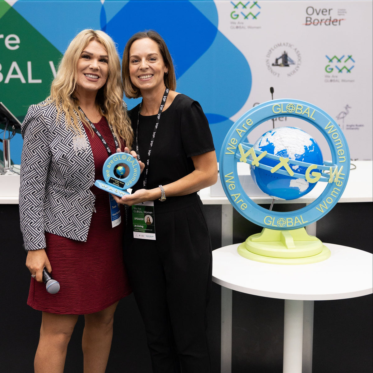 Two women holding an award in front of a 'Global Women' display.
